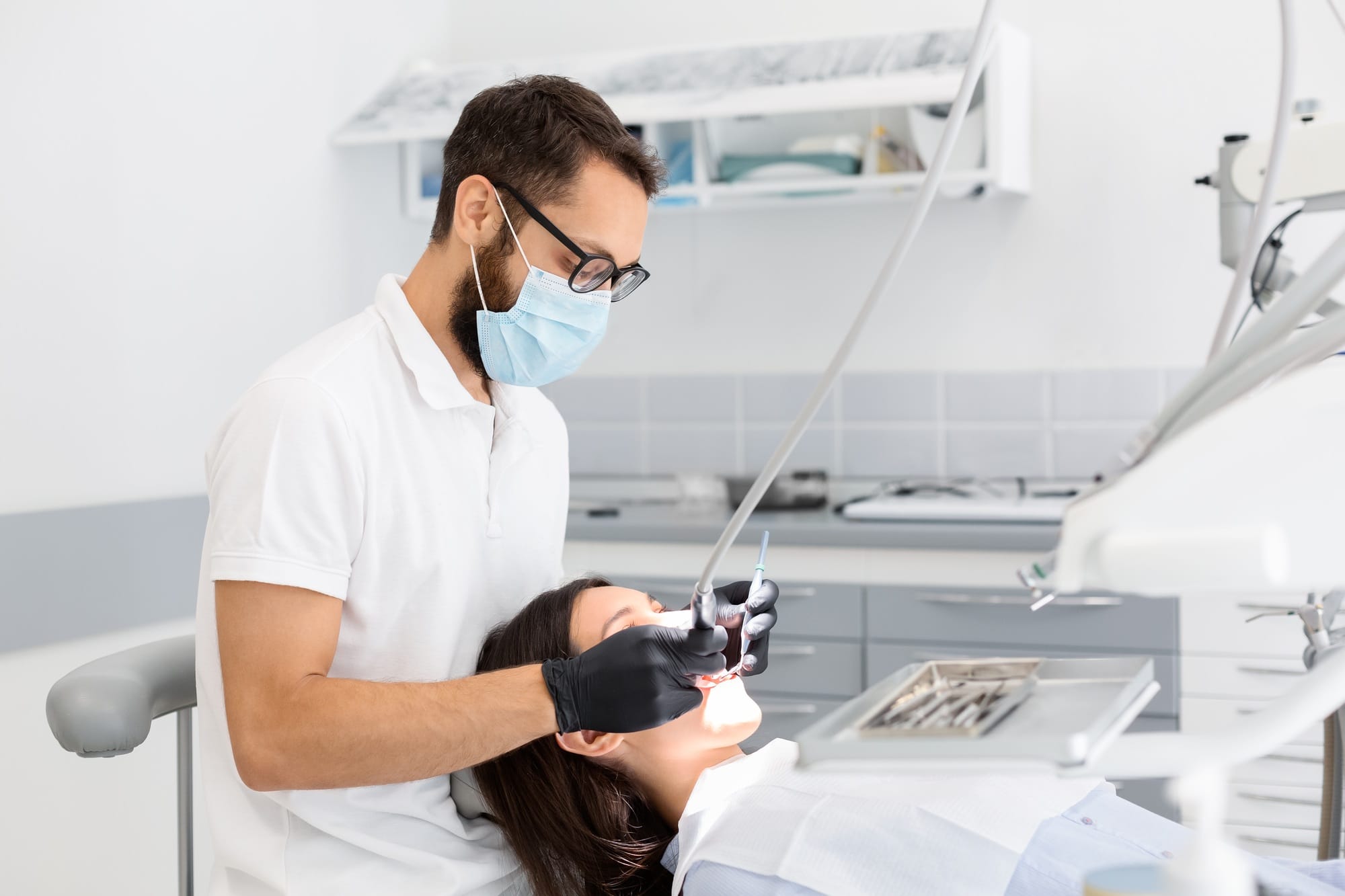 Dentist doctor in glasses filling teeth to female patient Dentist doctor in glasses filling teeth to female patient