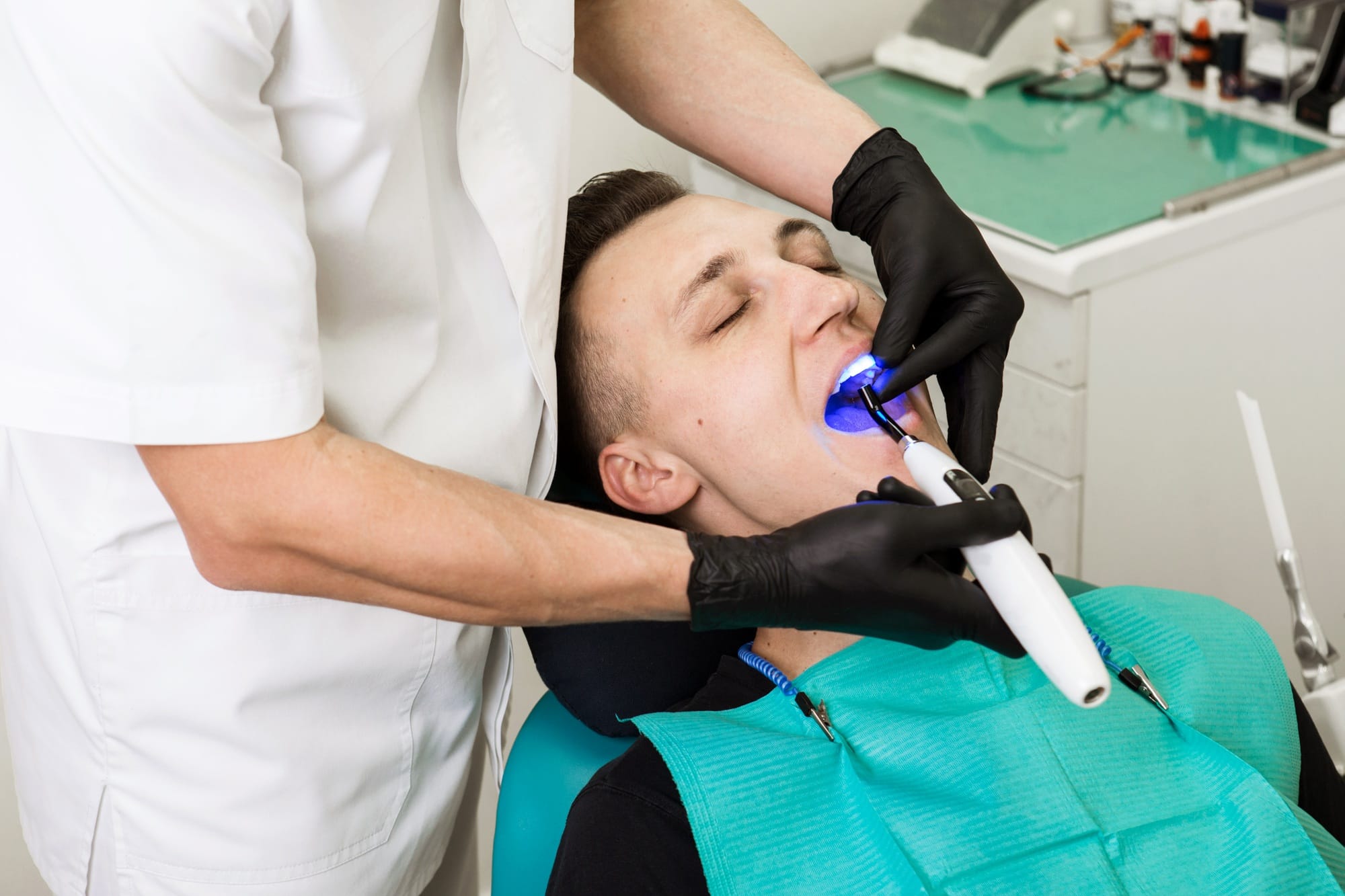 Dentist shine a bright blue Light in the male patient's mouth to harden composite filling. Dental Dentist shine a bright blue Light in the male patient's mouth to harden composite filling. Dental