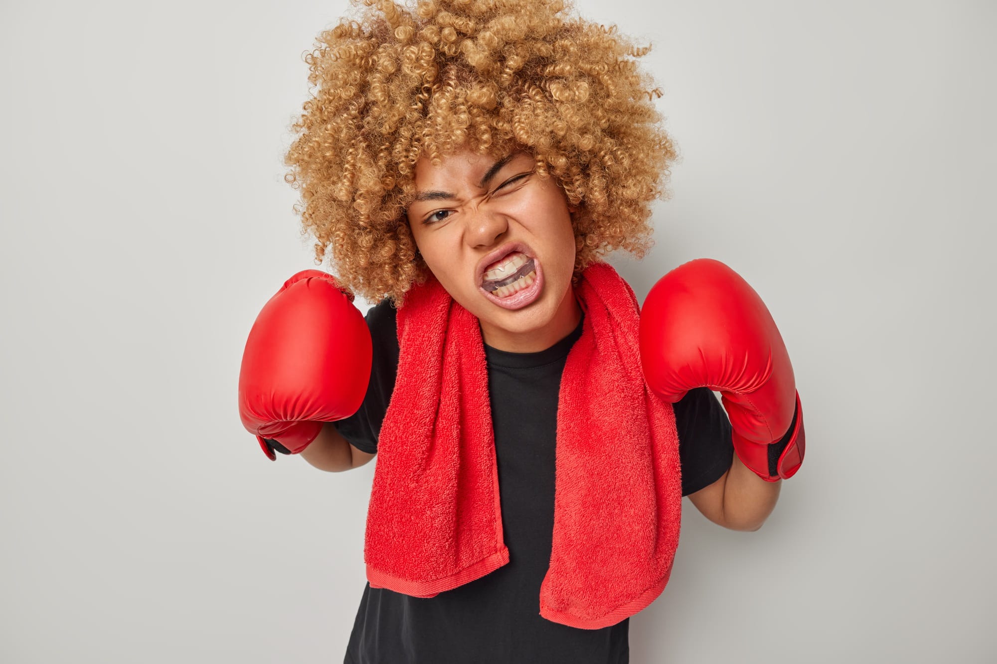 Indoor shot of curly haired female boxer protects teeth with mouthguard ready for fight wears black Indoor shot of curly haired female boxer protects teeth with mouthguard ready for fight wears black