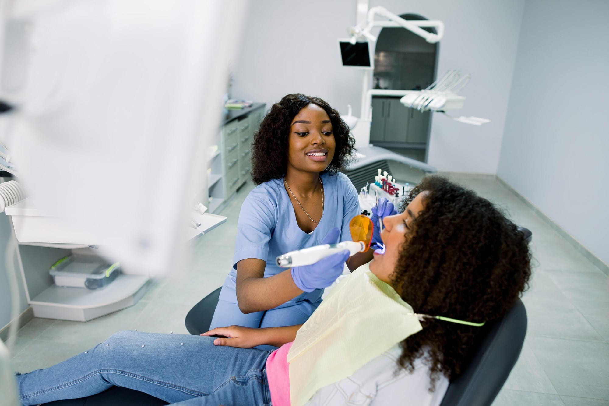 Smiling black woman dentist wearing blue uniform, providing tooth restoration Smiling black woman dentist wearing blue uniform, providing tooth restoration