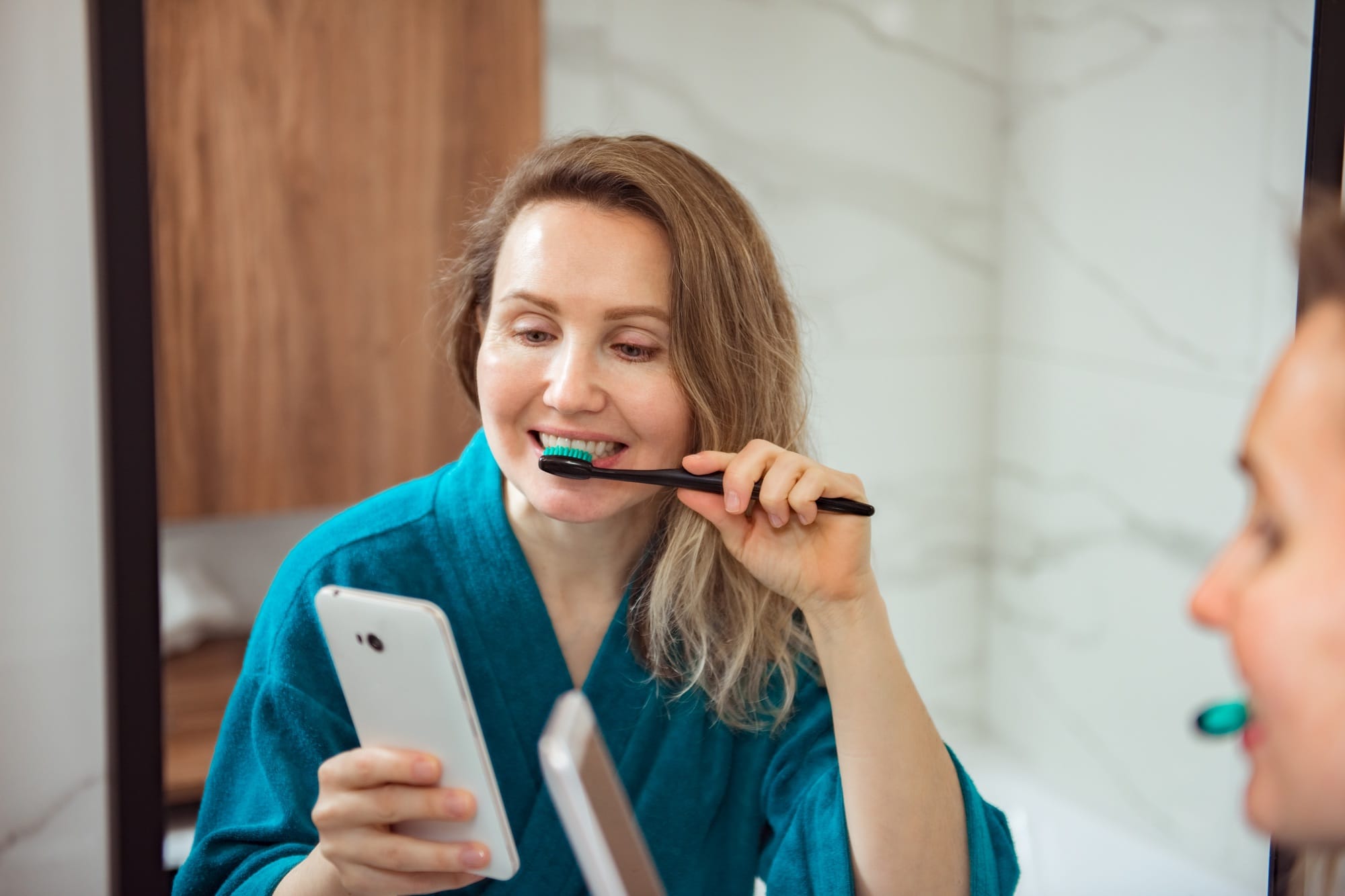 Social media affect. Young happy woman brushing teeth and looking at phone screen Social media affect. Young happy woman brushing teeth and looking at phone screen
