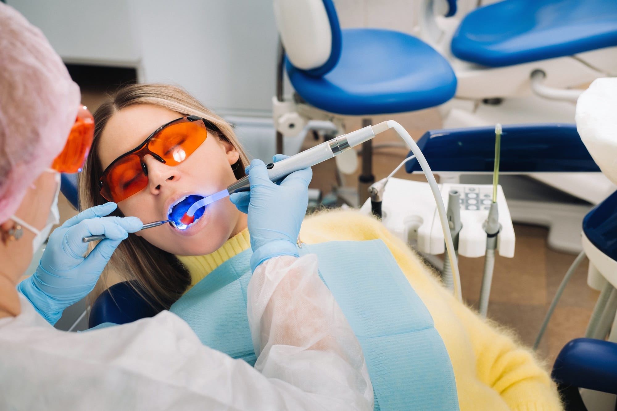 A young beautiful girl in dental glasses treats her teeth at the dentist with ultraviolet light A young beautiful girl in dental glasses treats her teeth at the dentist with ultraviolet light