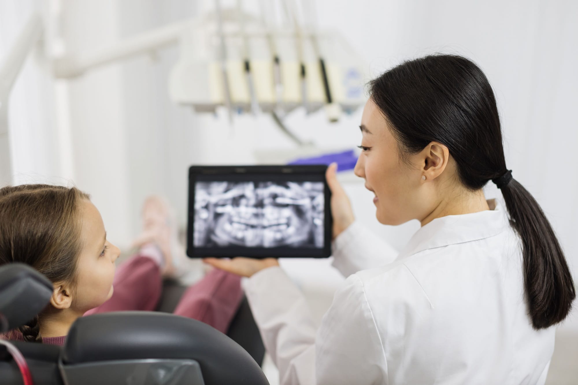 Back view of smiling happy caucasian child girl visiting dentist, sitting in dental chair Back view of smiling happy caucasian child girl visiting dentist, sitting in dental chair