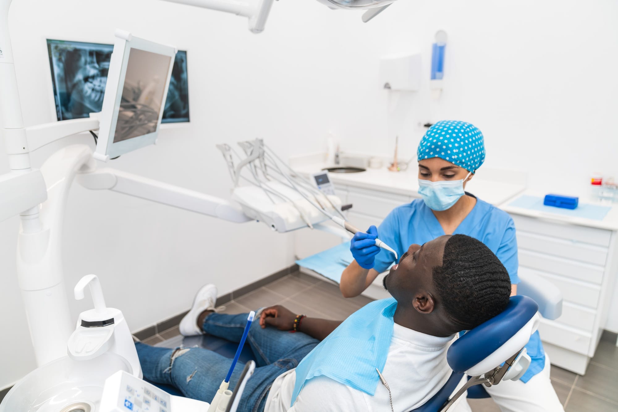 Dental hygienist performing a dental cleaning procedure on an African male patient in the clinic. Dental hygienist performing a dental cleaning procedure on an African male patient in the clinic.