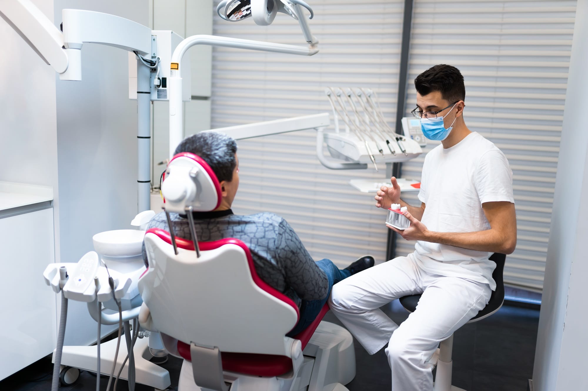 Dental surgeon with dental crown in hands model talks to patient about prosthetics. Dental surgeon with dental crown in hands model talks to patient about prosthetics.