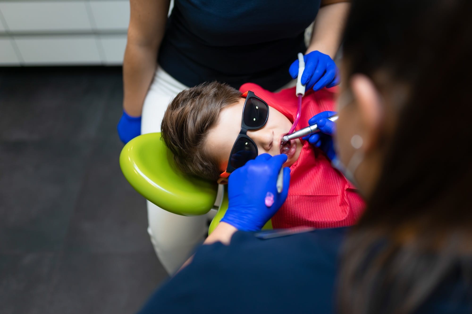 Dentist and assistant make preventive dental plaque cleaning for teenager Dentist and assistant make preventive dental plaque cleaning for teenager