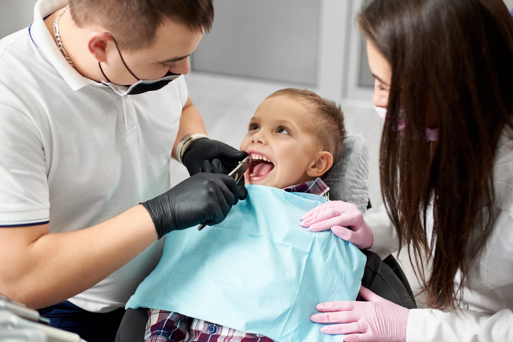 Dentist and assistant pull the tooth to the baby with forceps. Dentist examining and filling teeth patients in clinic for better dental health and a bright smile.