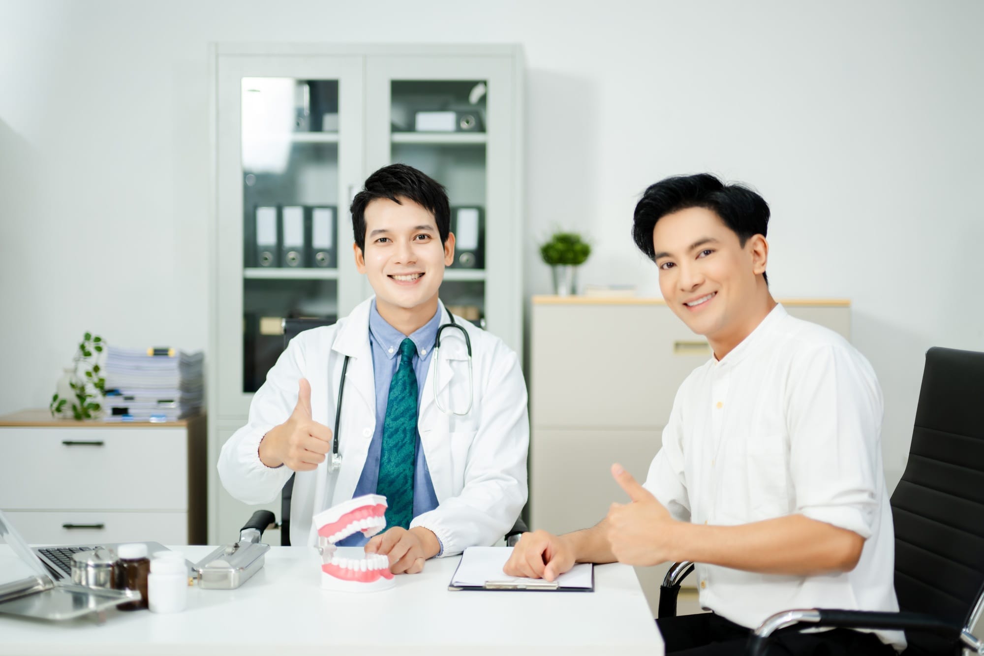 Dentist explaining dental care to male patient using a tooth model. Health consultation, Dentist explaining dental care to male patient using a tooth model. Health consultation,