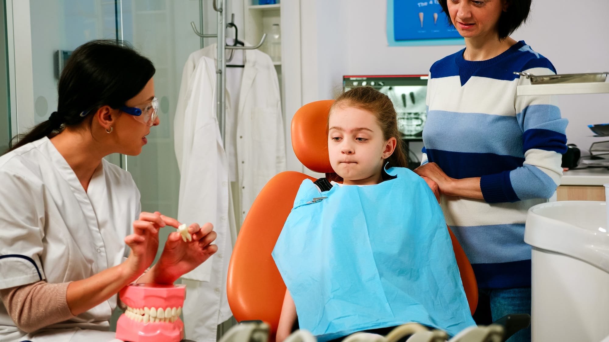 Dentist explaining to girl procedure of extraction using model of dental teeth Dentist explaining to girl procedure of extraction using model of dental teeth