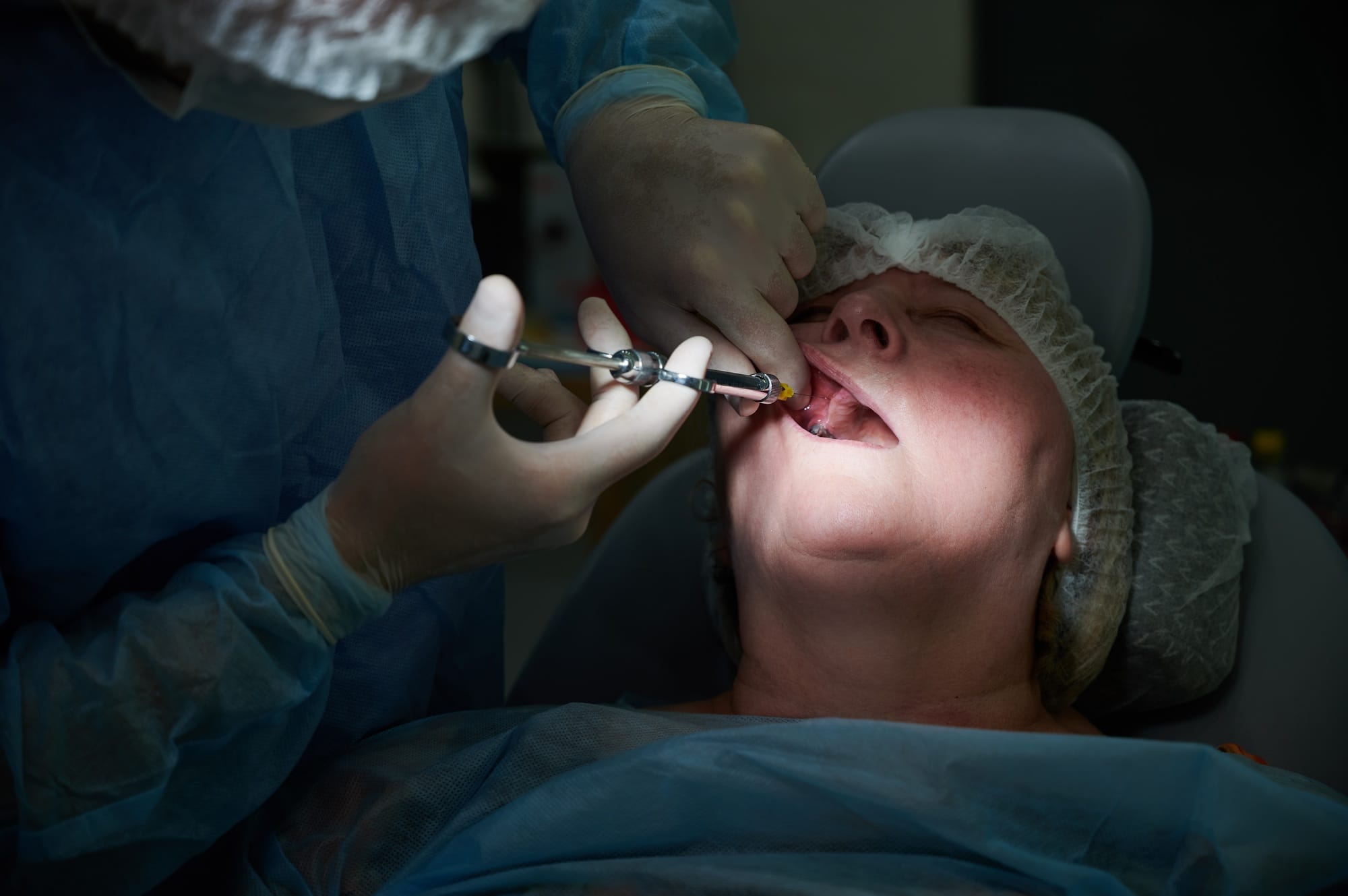 Dentist injecting anesthetic medicine into patient inner cheek or gum.