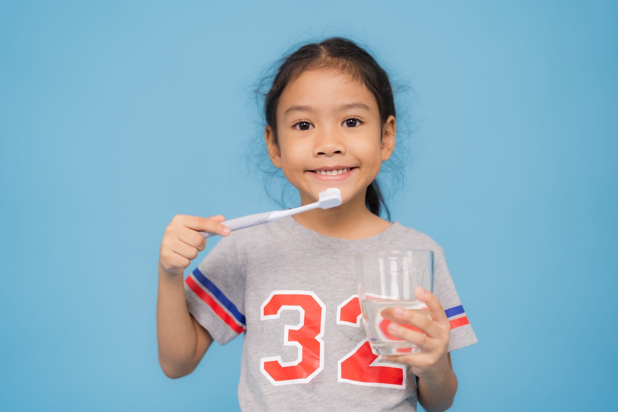 Happy little girl brushing teeth and holding glass of water Happy little girl brushing teeth and holding glass of water