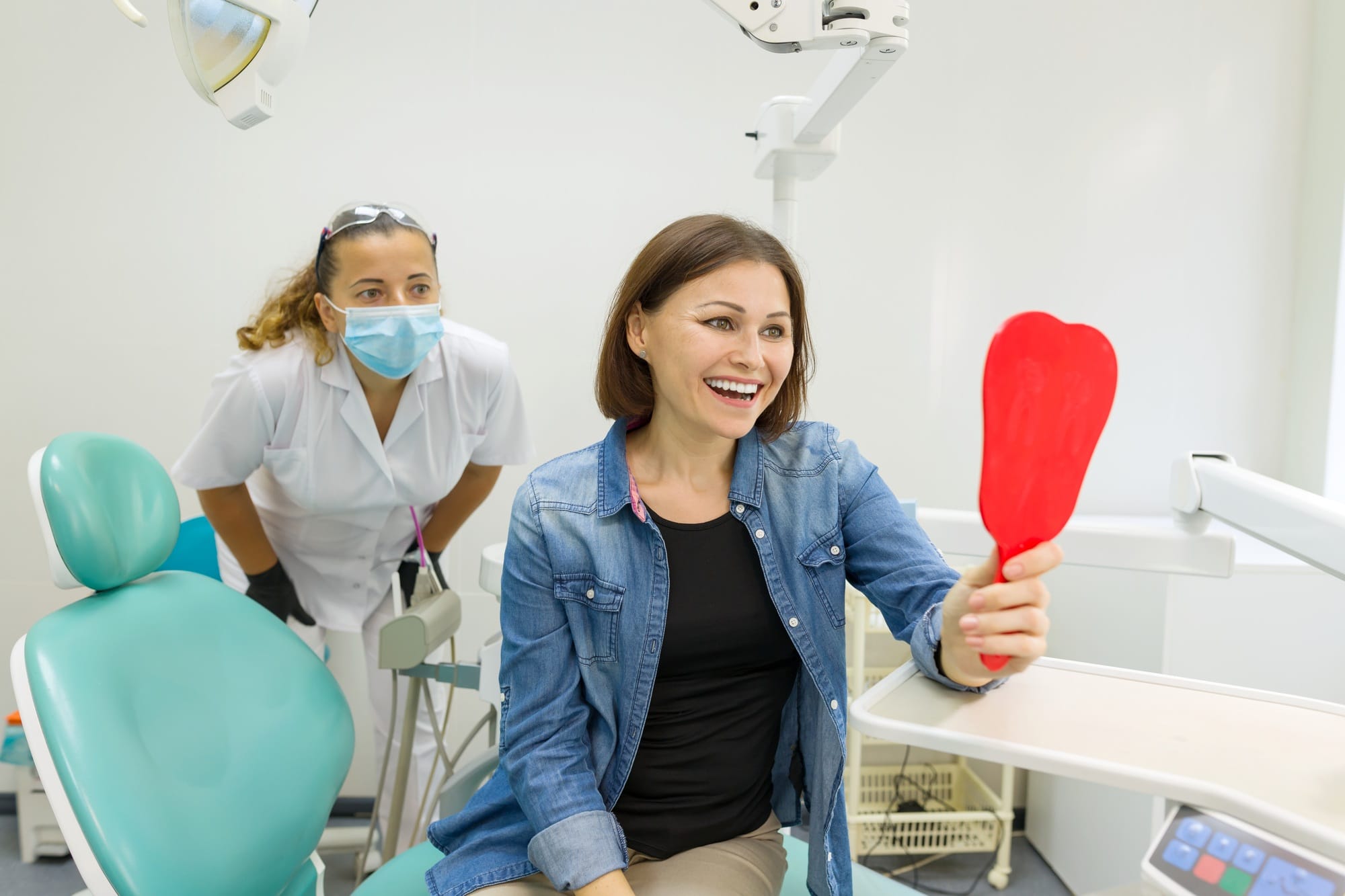 Happy woman patient looking in the mirror at the teeth, sitting in the dental chair Happy woman patient looking in the mirror at the teeth, sitting in the dental chair