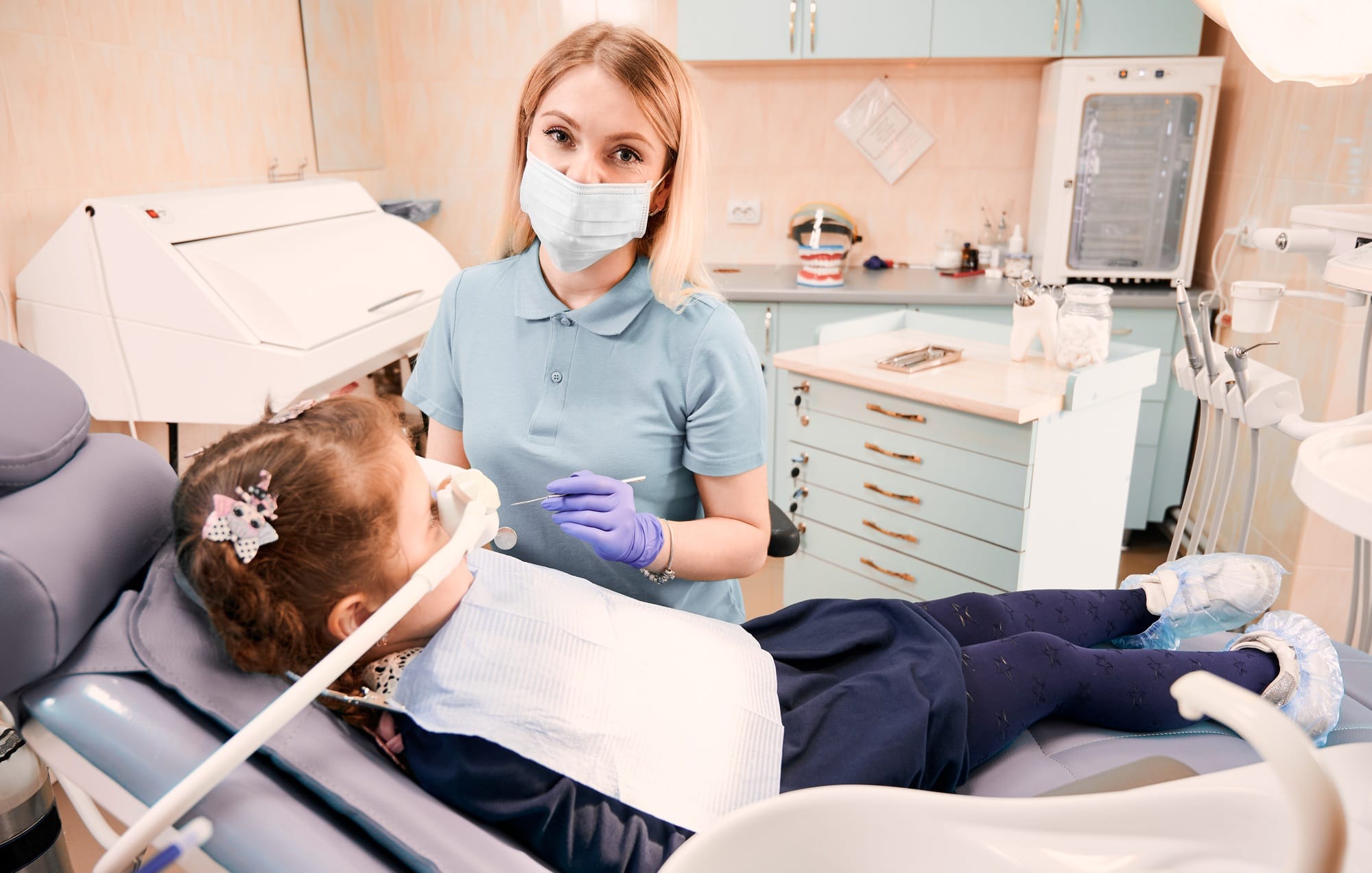 Pediatric dentist examining little girl teeth in dental office.