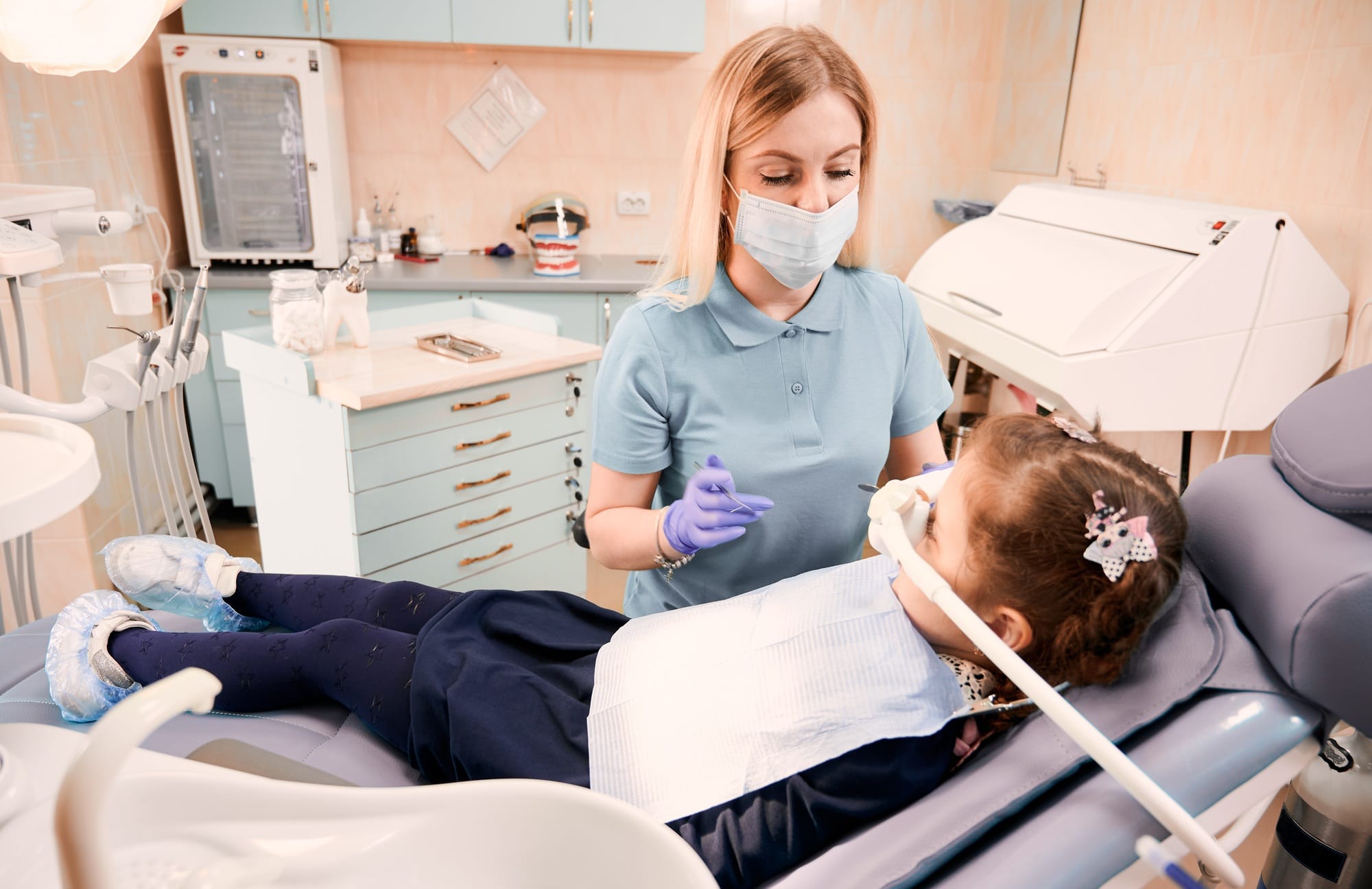 Pediatric dentist examining little girl teeth in dental office.