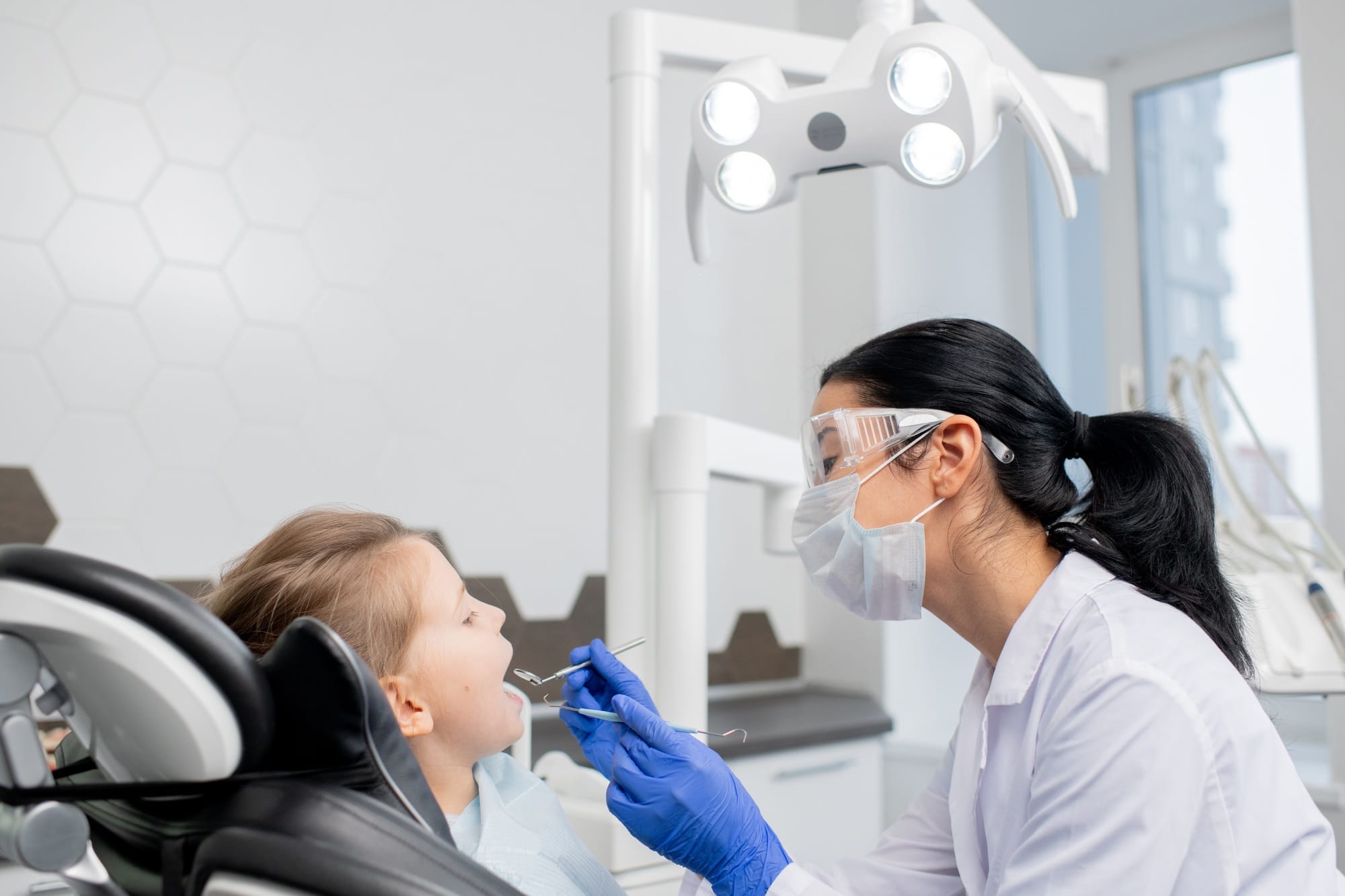 Young female dentist going to do oral checkup of oral cavity of little patient Young female dentist going to do oral checkup of oral cavity of little patient