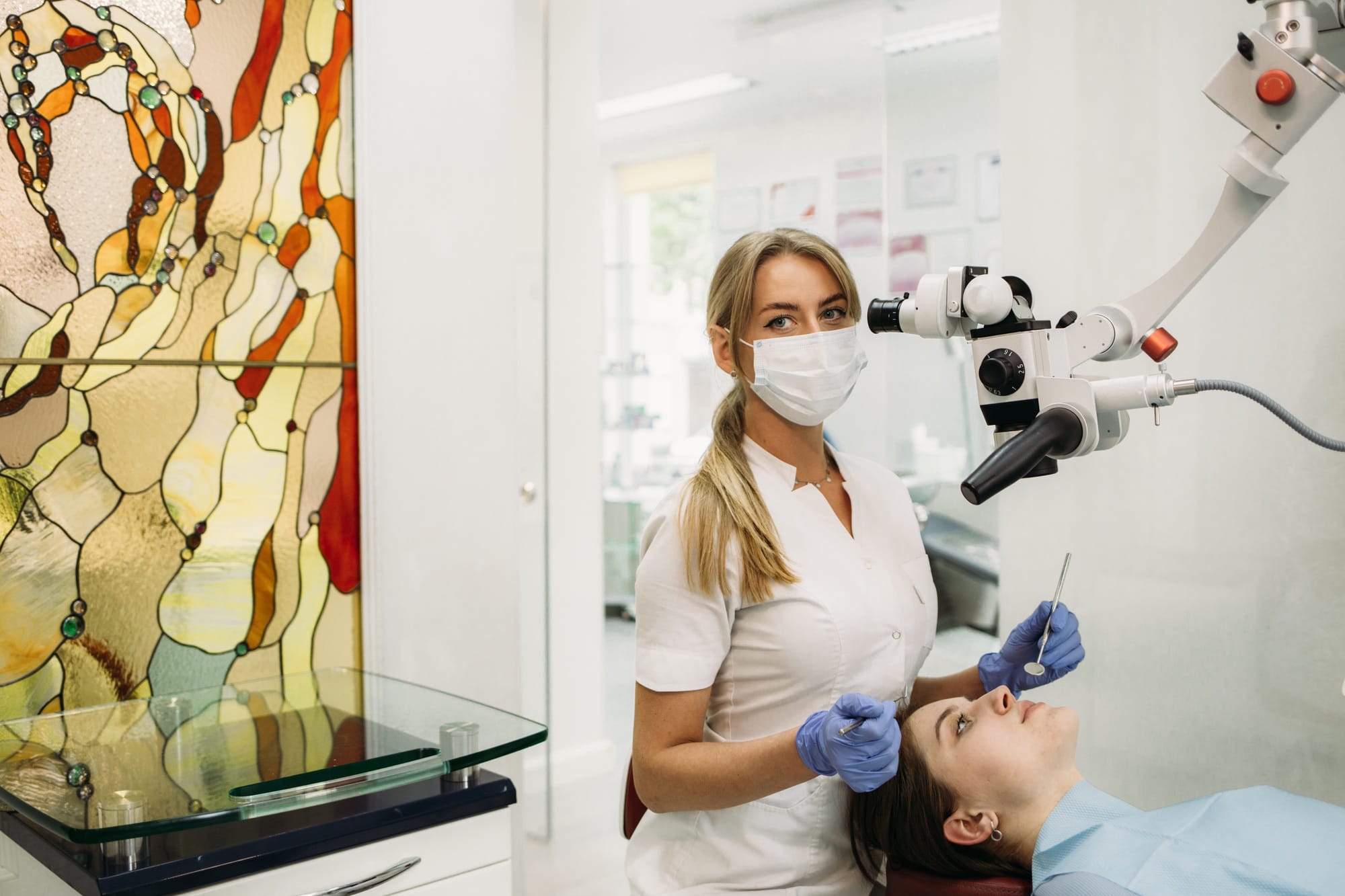 Young woman dentist treating root canals using microscope in the dental clinic. Man patient lying on