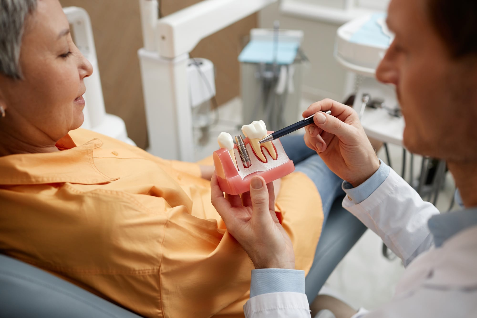 Closeup of male dentist explaining dental implant surgery to patient in clinic Closeup of male dentist explaining dental implant surgery to patient in clinic
