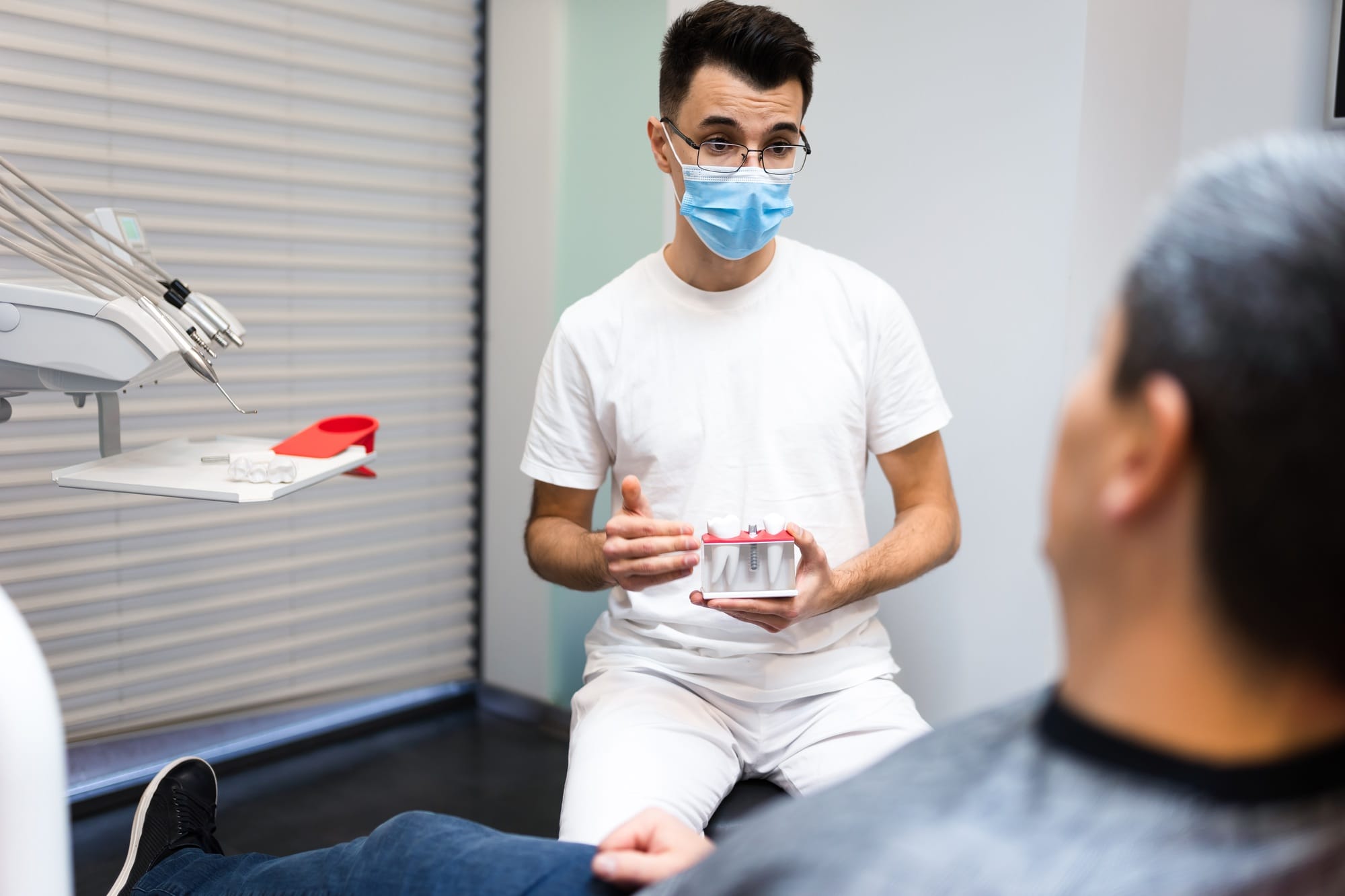 Dental surgeon with dental crown in hands model talks to patient about prosthetics. Dental surgeon with dental crown in hands model talks to patient about prosthetics.