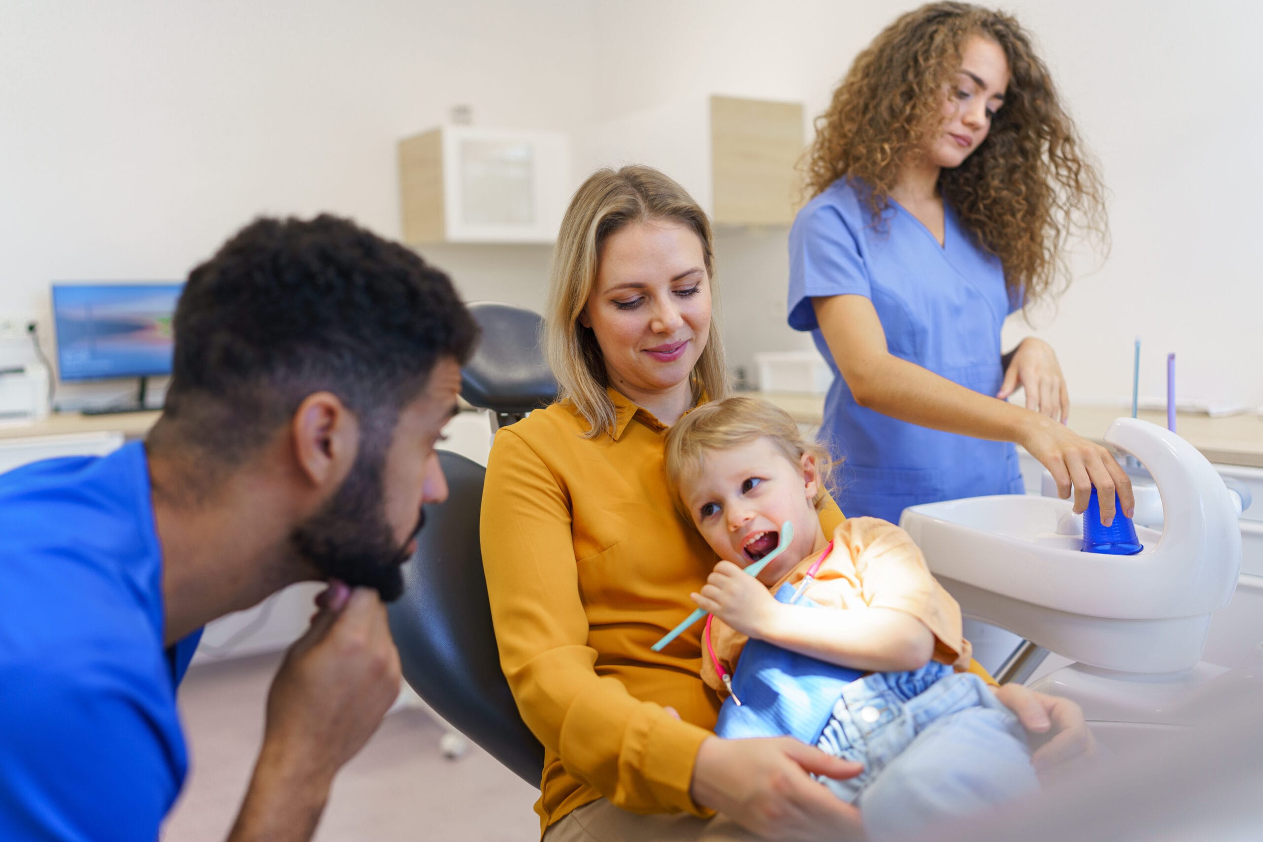 Little girl sitting with her mother on dentist chair, during preventive examination. Oral surgeon performing surgery installing implant