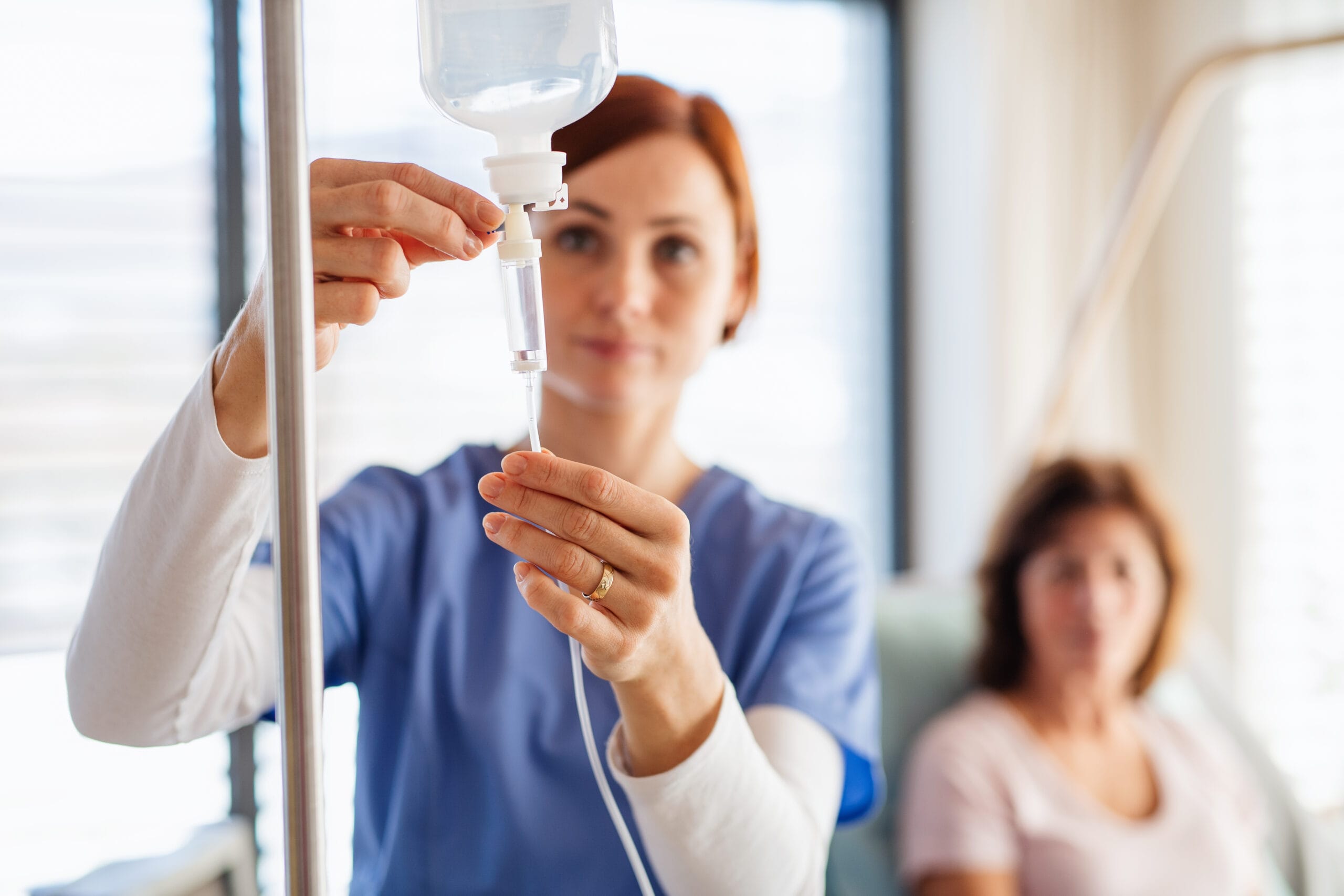A nurse with IV drip and patient in bed in hospital room. Partial view of a nurse holding dentures in hands