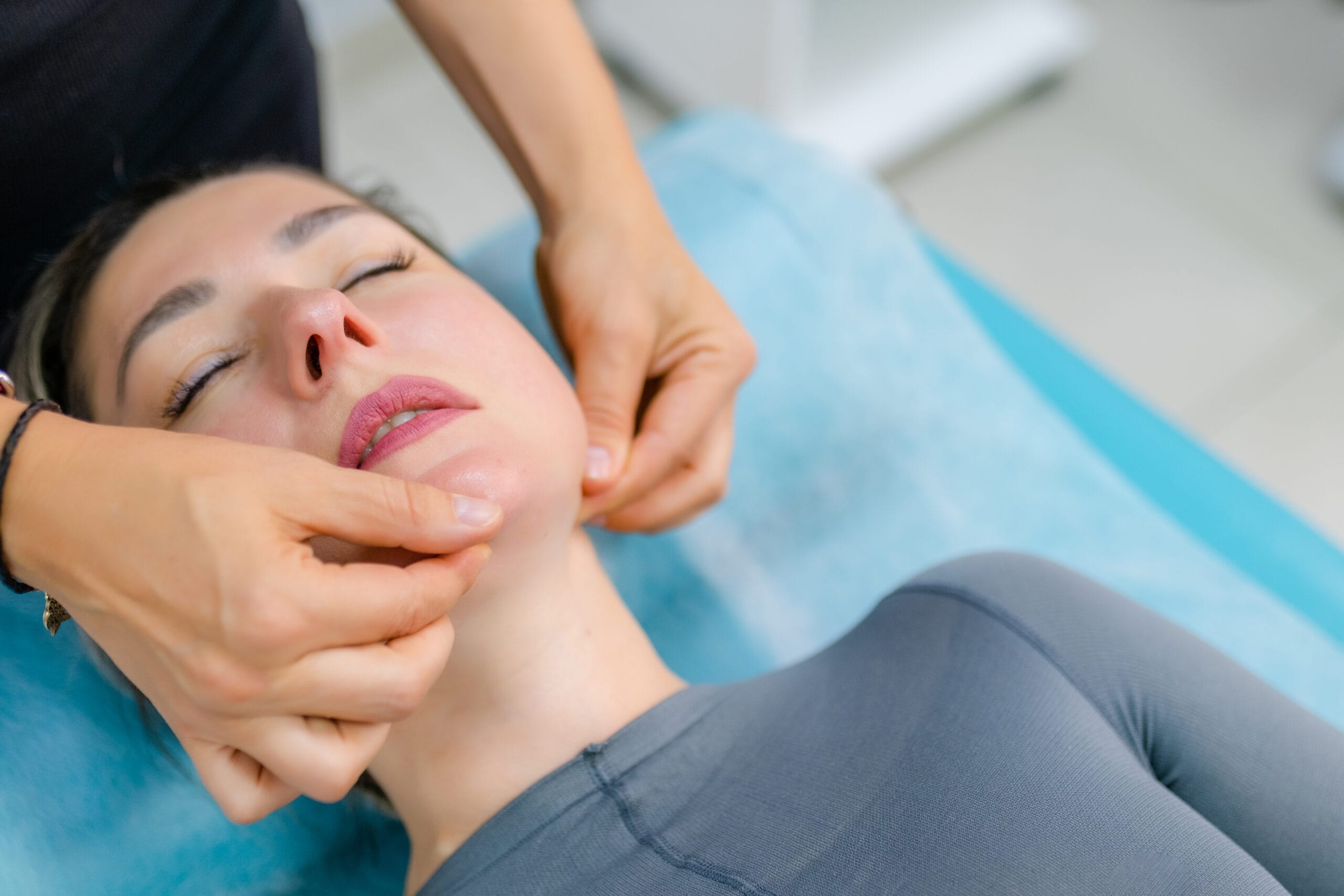 unidentified young woman masseur doing facial massage to young client woman Smiling attractive male patient holding mirror, looking, talking to senior professional dentist